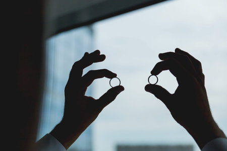 Groom holds pair of wedding rings on the background of window. Dark tone.の写真素材
