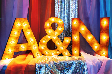 Fashion design element for wedding ceremonies, banquets, parties decoration - wooden letters (first letters in names of bride and groom) with light bulbs and sparkling fabric.の写真素材