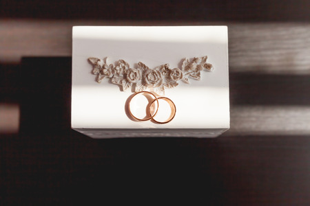 Pair of golden wedding rings with diamonds on white shabby decorative box. Beautiful symbol of love and marriage.の写真素材