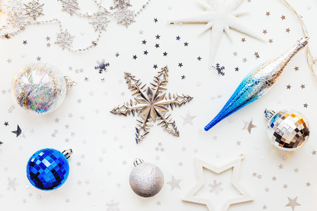 Christmas and New Year holiday background with decorations and light bulbs. Silver and blue shining balls, white snowflakes and star confetti. Flat lay, top view.の写真素材