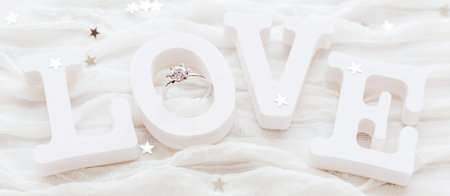 Word LOVE on white fabric background with engagement diamond ring. Good for Valentine's day cards....