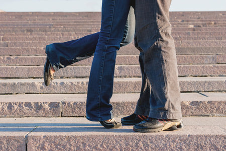 Young couple hugging on stone staircase steps. Woman flirty lifted her leg. 