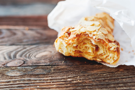 Tasty croissant in white paper bag on table. Rustic wooden background with sweet dessert. の写真素材