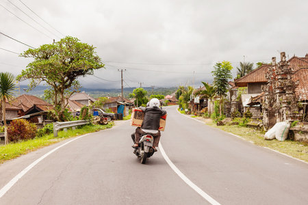BALI, INDONESIA - January 30, 2013. Men carry a stereo on a bike. Driver driving motorcycle through village.のeditorial素材