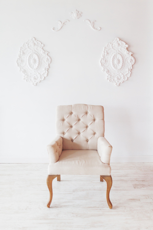 Beige chair on white wall background with swirl decorations. Studio interior.の写真素材