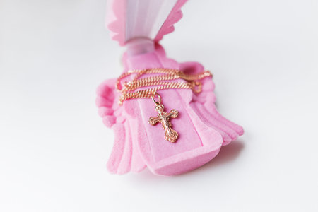 Golden cross for christening on pink gift box in shape of praying angel. Elegant religious accessory for little baby girl. Russian Orthodox church ceremony details.の写真素材