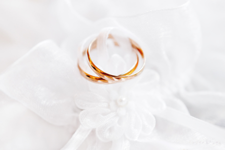 Pair of golden wedding rings on lace silk fabric with fabric flower. Wedding embroidery dress detail.の写真素材