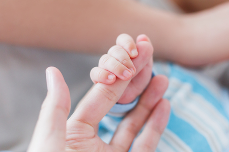 Newborn baby holding his mother finger. Hands  of tiny baby and adult woman. Moment of tenderness.の写真素材