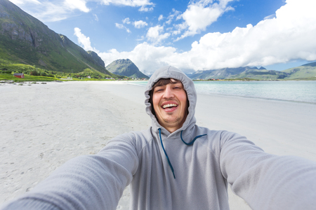 Tourist man making selfie on Rambergstranda beach on Lofoten islands. Beautiful sandy beach and azure water. Norway.の写真素材
