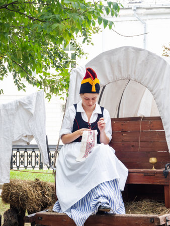 MOSCOW, RUSSIA - August 19, 2018. Woman dressed as a French peasant embroidering something. Annual festival Times and Epochs. Historical reconstruction of 19th century.のeditorial素材