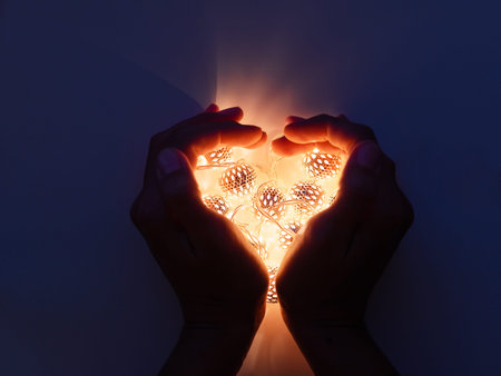 Hands with light bulbs in shape of heart. Metal light bulbs with delicate pattern shine in dark....