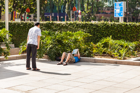 KUALA LUMPUR, MALAYSIA - February 01, 2013. Tourists take pictures of each other on the background of Petronas towers. Sometimes they have to lie down on sidewalk to include both  man and skyscraper in  frame.のeditorial素材