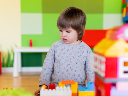 Toddler boy is playing in kidsroom with colorful constructor. Educational toy block in his hands. Kid is busy with toy bricks.の写真素材