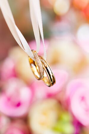 Golden wedding rings on bridal bouquet with pink and yellow roses. Traditional floral composition for wedding ceremony. Romantic symbol of love and marriage.の写真素材