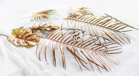 Artificial golden Monstera and fern leaves on white fabric.Graceful background with fake plants and folded textile. Cozy still life backdrop.の写真素材
