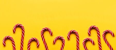 Banner with Christmas candy cones on yellow background. Colorful holiday sweets with bright copy space. Traditional dessert wtih red and white stripes.の写真素材