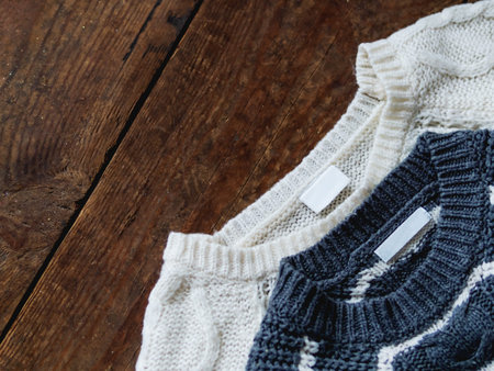 Grey and white knitted sweaters on shabby wooden background. Garment with clear labels.  Top view,...