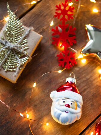 Christmas and New Year background with decorative Santa Claus, snowflakes and present with golden feather. Holiday decorations with light bulbs on wooden background.の写真素材