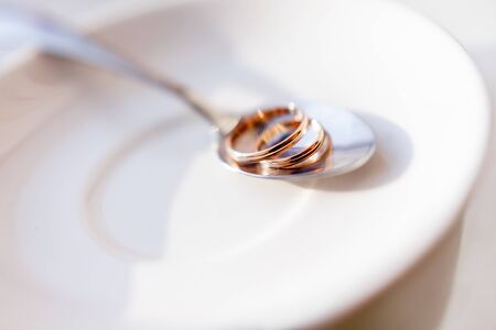 Golden wedding rings on shiny spoon. Traditional symbol of love and marriage on white plate.の写真素材