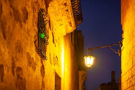 Narrow streets of Mdina, ancient capital of Malta. Night view on illuminated buildings and wall decorations of ancient town.の写真素材