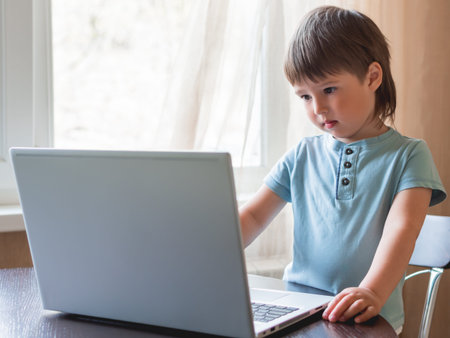 Curious toddler boy explores the laptop and presses buttons on computer keyboard.