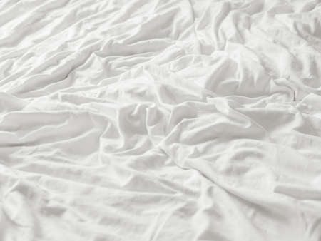 Background with white crumpled bed sheet. Creased soft linen with copy space. Unmade bed in bedroom of cozy home.の写真素材