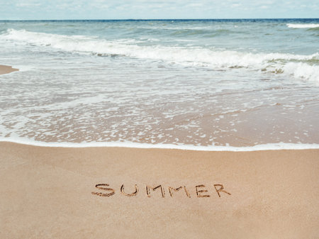 Sea coast with soft surf. Word SUMMER written on sandy beach. Summer vacation on seaside.の写真素材