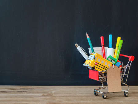 Colorful stationery and school bus model in shopping cart. Back to school concept. Blackboard background with copy space on price tag. School shopping.の写真素材
