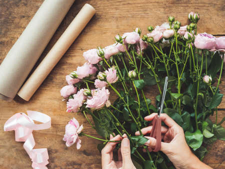 Top view on wooden table with roses, scissors, craft paper and pink ribbon on it. Florist work place. Accessories for making bouquets and floral compositions.の写真素材