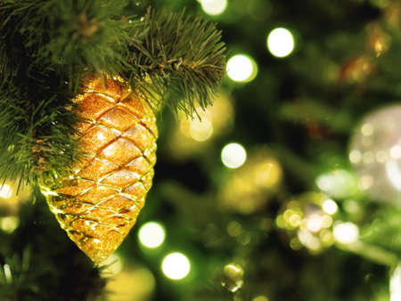 Decorative golden pine cone on Christmas tree. Festive background with light bulbs. New Year celebration.の写真素材