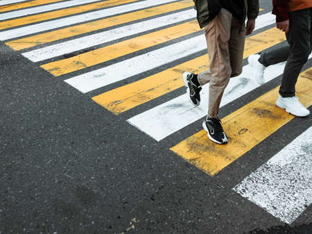 Two young man cross the road at a pedestrian crossing. White and yellow stripes on asphalt - zebra crossing. Traffic sign. City road marking.の写真素材