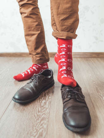 Young man in chinos trousers and bright red socks with reindeers on them is ready to wear suede shoes. Scandinavian pattern. Winter holiday spirit. Casual outfit for New Year and Christmas celebration.の写真素材