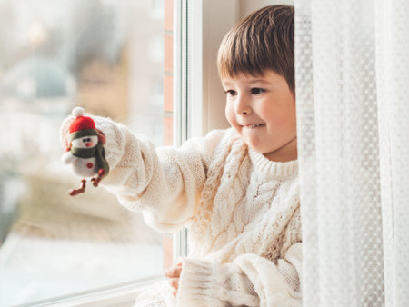 Kid with felt decorative snowman for Christmas tree. Boy in cable-knit oversized sweater. Cozy outfit for snuggle weather. Funny character with red Santa Claus hat. Winter holiday spirit. New year.の写真素材
