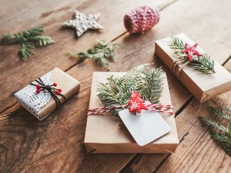 Christmas DIY presents wrapped in craft paper with fir tree twigs. Red decorations in shape of Christmas tree, stars. New Year gifts on wooden background. Winter holiday spirit.の写真素材