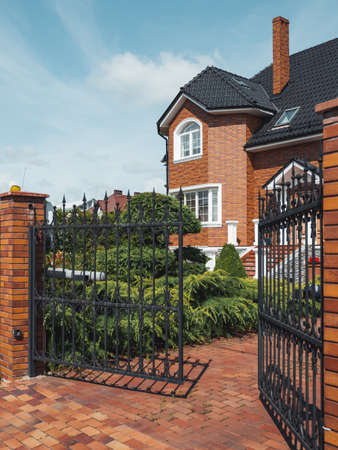 Gate is open to territory of house in suburbs of Kaliningrad. Well-kept brick building with manicured lawns. Russia.の写真素材