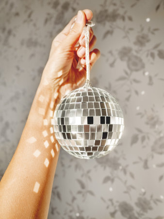 Woman holds sparkling on sun mirror disco ball. Light and shadow. Sunny morning at home. Sun...