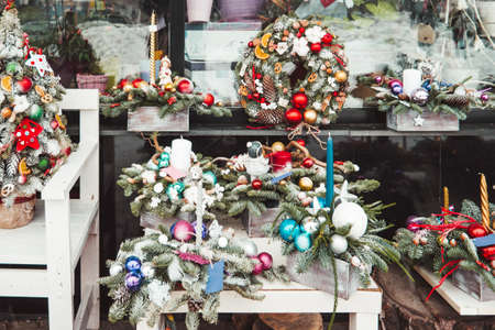 Small decorated Christmas trees decorated are on sale in flower shop window. Wreaths and decoration for New Year celebration. Winter holiday spirit.の写真素材