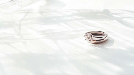 Wedding and engagement rings with diamond. Symbol of love and marriage on white background with laced shadow. Sunlight on white background.の写真素材