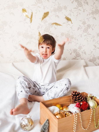 Joyful boy is playing with decorations for Christmas tree. Funny kid is ready for New Year celebration. Cozy home. Winter holiday spirit.の写真素材