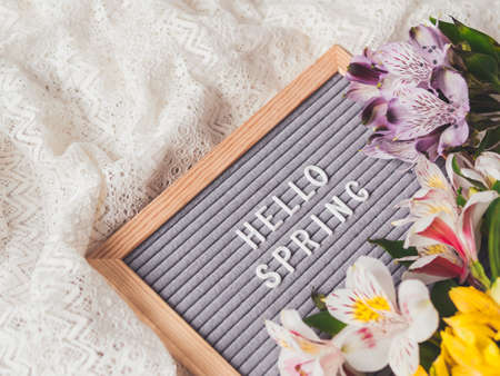 Letter board with season greeting HELLO SPRING on laces white textile background with fresh alstroemeria flowers.の写真素材