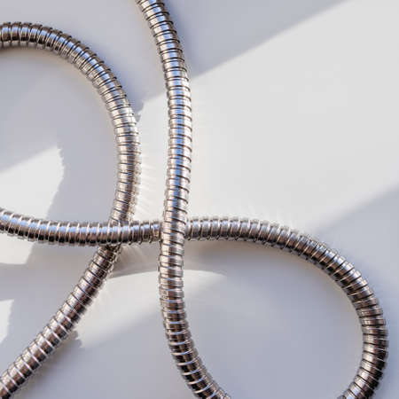 Metal shower hose on white background. Flexible chrome tube. Corrugated plumbing tube on geometrical square banner with copy space on hard sunlight and shadow.の写真素材