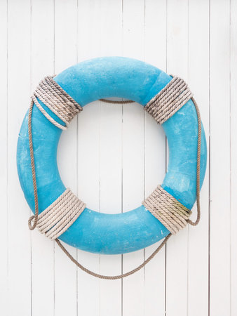 Blue lifebuoy with rope on white wooden background. Symbol of travel and vacation. Rescue device.