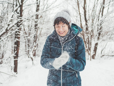 Smiling woman is playing with snow. Fun in snowy winter forest. Woman laughs as she walks through wood. Sincere emotions.の写真素材