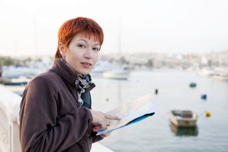 Woman with short red haircut reads Malta map. Curious woman stands near Msida Yacht Marina. Europe...