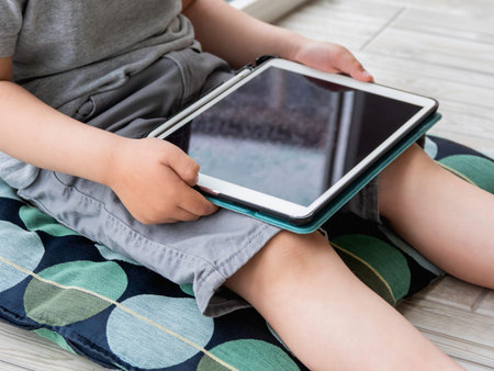 Curious boy watch cartoons on digital tablet. Kid sits on floor and uses electronic device. Indoor leisure for children while it's raining outside.の写真素材