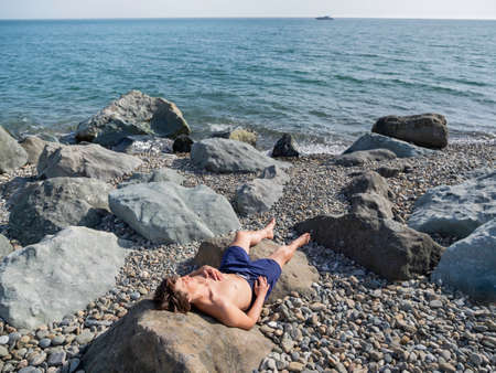 Man is sunbathing on rocks after swimming in sea. Healthy outdoor recreation. Vacation on sea coast. Seascape at sunny day.の写真素材