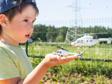 Little boy holds toy helicopter in front of real one on helipad. Kid dreams of becoming a pilot. Planning future in childhood.の写真素材
