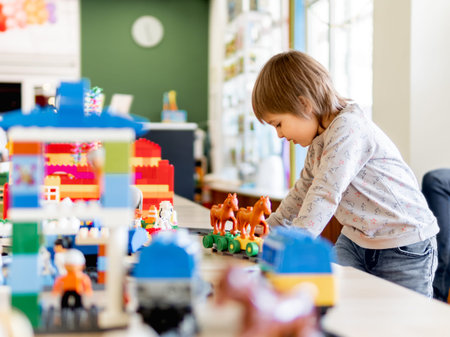 Toddler plays with colorful toy blocks. Little boy stares on figure from toy constructor. Interior of kindergarten or nursery. Indoors leisure activity for children.の写真素材