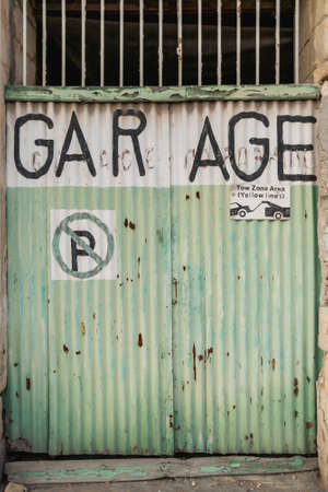Old battered garage doors. Signs warning about prohibition of parking and evacuation of parked cars. Gzira, Malta.の写真素材