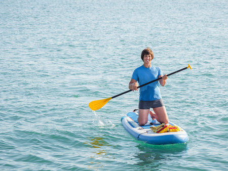 Handsome paddle boarder. Sportsman on knees paddling on stand up paddleboard. SUP surfing. Active...